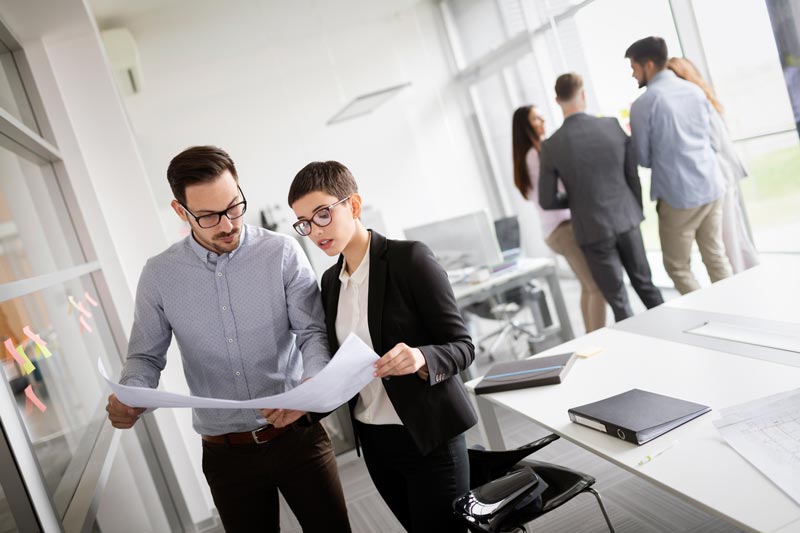 2 personnes regardent un document devant un groupe de personne
